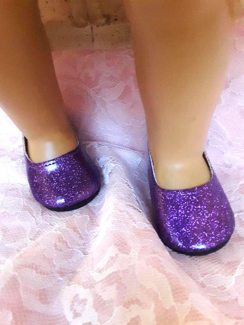 May include: A pair of purple glitter shoes with a shiny finish. The shoes are flat and have a rounded toe.
