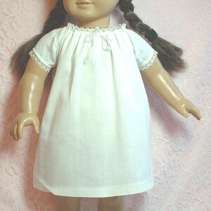 May include: A white doll wearing a white camisole with lace trim and brown sandals. The doll has long brown hair in braids and brown eyes. The doll is standing on a pink background.
