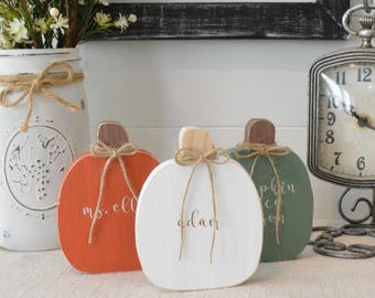 Peut inclure: Trois décorations en forme de citrouille en bois plat, de couleurs orange, blanc et vert sauge. Chaque citrouille possède une tige en bois naturel, un nœud en ficelle de jute et une inscription blanche en cursive. On peut lire "ms. ell", "adam" et "pumpkin spice season".