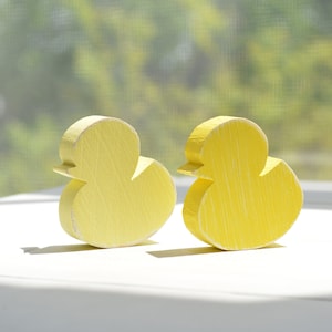 May include: Two yellow wooden duck figurines, one facing left and the other facing right, on a white surface.