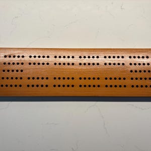 May include: A wooden cribbage board with a natural wood finish and a grid of holes for scoring.