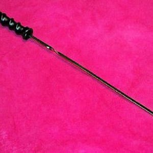 May include: A black and silver metal dipstick with a twisted handle. The dipstick is on a pink surface.