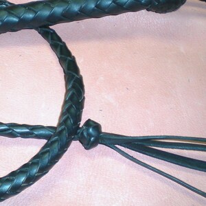 May include: A black leather braided whip with a knot at the end and three leather tassels.