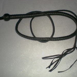 May include: A black leather bullwhip with a braided handle and a long tassel. The whip is coiled and laid out on a white surface.