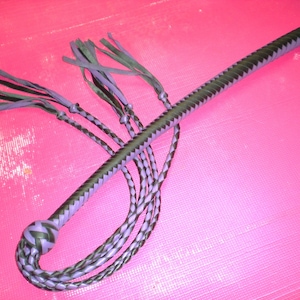 May include: A black and purple leather whip with multiple strands and a braided handle. The whip has a tassel at the end.