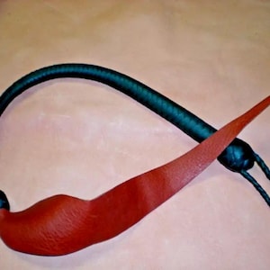 May include: A black leather whip with a red leather tassel. The whip is coiled and the tassel is hanging down.