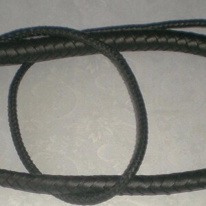 May include: A black leather bullwhip with a braided design. The whip is coiled and ready for use.