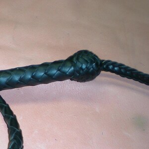 May include: A black leather braided whip with a knotted handle.