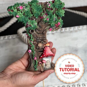 Pode incluir: Uma decoração de biscoito artesanal e detalhada que representa uma árvore com um rosto caprichoso, flores cor-de-rosa e um cogumelo vermelho e branco. O biscoito está em um palito e tem uma etiqueta que diz "Cookies Studio Video Tutorial passo a passo Qualidade Premium".