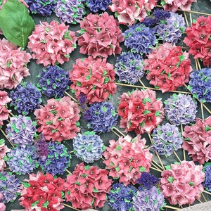 May include: A collection of pink and purple hydrangea flower arrangements on sticks. The flowers are arranged in a circular pattern on a dark gray surface.