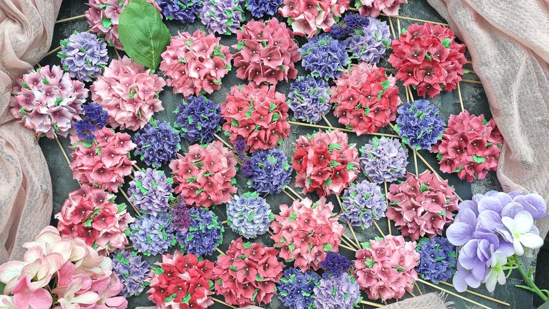 May include: A collection of pink and purple hydrangea flower arrangements on sticks. The flowers are arranged in a circular pattern on a dark gray surface.