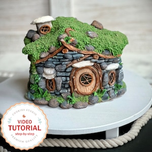 May include: A miniature stone house with a green moss roof, a round door, and a small chimney. The house is made of gray stones and has a rustic, whimsical look.