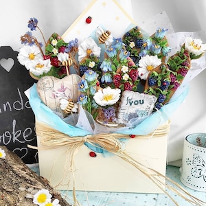 May include: A white envelope box filled with a bouquet of colorful sugar cookies decorated with flowers, leaves, and bees. The cookies are arranged in a vase and the box is tied with a brown ribbon. The box has a "For You" tag attached to it.