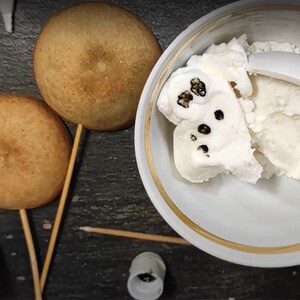 May include: Two round, brown, cake pops on wooden sticks, and a white bowl with a scoop of white ice cream with black specks.