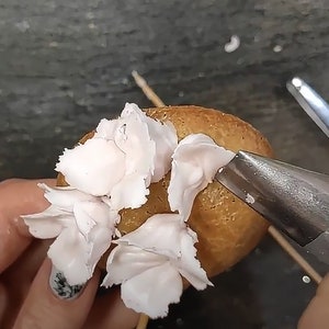 May include: A close-up of a piping bag being used to decorate a round cake with pink frosting. The frosting is piped in a flower shape.
