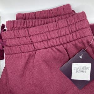 Może przedstawiać: Bordowe spodnie dresowe ze sznurkiem w kolorze białym i metką z napisem "Burgundy/X4ZZM".