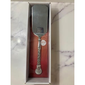 May include: A stainless steel cake server with an ornate handle. The server is in a white box with a red interior. The handle has a floral design and the text "18/10 Stainless Steel".