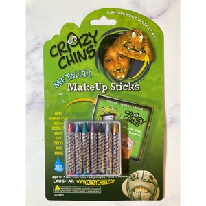 May include: A green and white pack of "Crazy Chins" metallic makeup sticks. The package contains six colourful sticks, a step-by-step booklet, and features the text "Turn Your World Upside-Down!" and "Laugh at: www.crazychins.com".