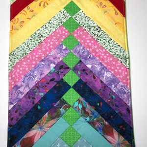 May include: A colourful quilt with a chevron pattern. The quilt is made of various fabrics with different patterns, including floral, geometric, and abstract designs. The quilt is in shades of green, red, yellow, pink, purple, blue, and teal.