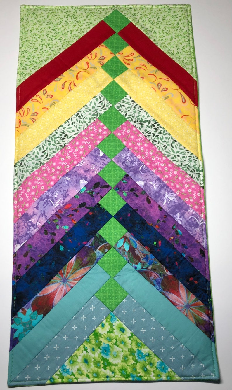 May include: A colourful quilt with a chevron pattern. The quilt is made of various fabrics with different patterns, including floral, geometric, and abstract designs. The quilt is in shades of green, red, yellow, pink, purple, blue, and teal.