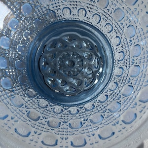 K&ouml;nnte beinhalten: Eine blaue Glassch&uuml;ssel mit einem dekorativen, rautenf&ouml;rmigen Muster. Die Sch&uuml;ssel hat eine erh&ouml;hte Mitte mit einem floralen Design.