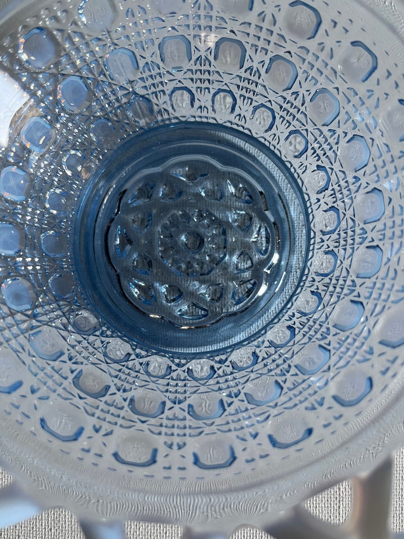 K&ouml;nnte beinhalten: Eine blaue Glassch&uuml;ssel mit einem dekorativen, rautenf&ouml;rmigen Muster. Die Sch&uuml;ssel hat eine erh&ouml;hte Mitte mit einem floralen Design.