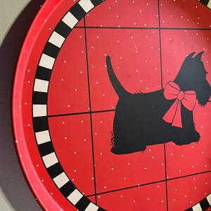 May include: A red metal serving tray with a black and white checkered border. The tray features a black silhouette of a dog with a red bow, set against a red background with white polka dots. The tray has a vintage aesthetic.