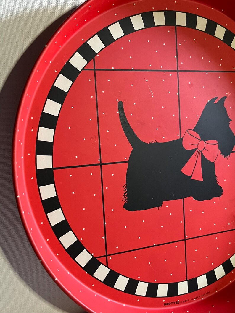 May include: A red metal serving tray with a black and white checkered border. The tray features a black silhouette of a dog with a red bow, set against a red background with white polka dots. The tray has a vintage aesthetic.