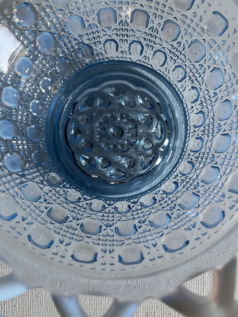 K&ouml;nnte beinhalten: Eine blaue Glassch&uuml;ssel mit einem dekorativen, rautenf&ouml;rmigen Muster. Die Sch&uuml;ssel hat einen gewellten Rand und eine erhabene Mitte.