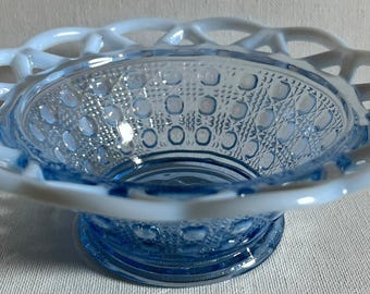 Puede incluir: Un cuenco de cristal azul claro con un borde blanco de estilo celosía y un patrón texturizado de cuadrados en relieve y rayado cruzado en las paredes interiores y exteriores. El cuenco se asienta sobre una base circular y tiene un acabado translúcido.