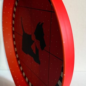 May include: Red, round decorative tray with a black silhouette of a dog wearing a red bow. The tray has a red rim with white polka dots and a black and white striped border.