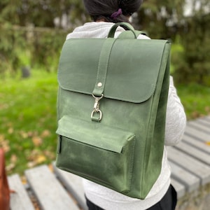 Peut inclure: Un sac à dos en cuir vert foncé avec une fermeture à rabat et une poche avant. Le sac à dos a une boucle argentée et des détails de couture.