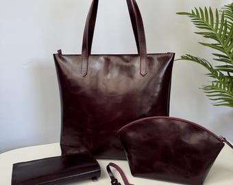 May include: A set of burgundy leather accessories, including a tote bag, a cosmetic bag, a wallet, and a tassel. The tote bag has long handles and a zipper closure. The cosmetic bag has a curved shape and a zipper. The wallet is rectangular. The tassel is attached to a leather strap.