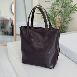 May include: A dark brown leather tote bag with two top handles. The bag has a smooth, polished finish.