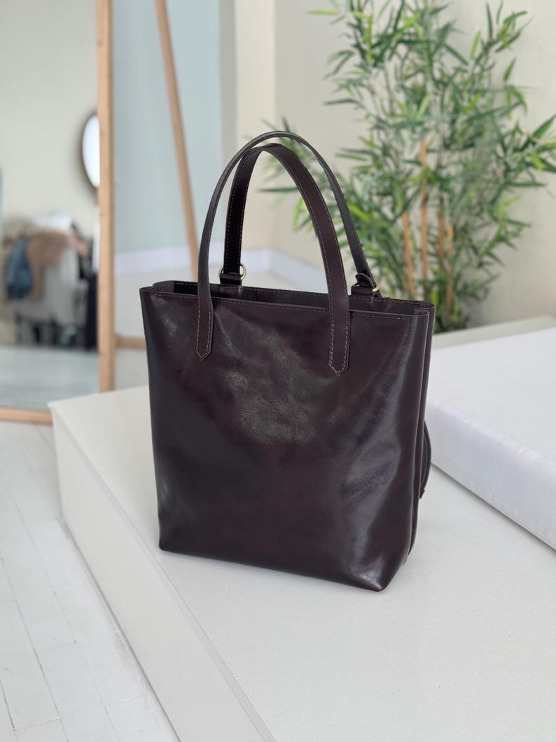 May include: A dark brown leather tote bag with two top handles. The bag has a smooth, polished finish.