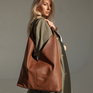 May include: A woman wearing a green trench coat carries a brown leather tote bag over her shoulder.