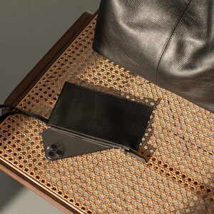 May include: A black leather tote bag and a black leather wallet with a zipper on a woven wicker chair.