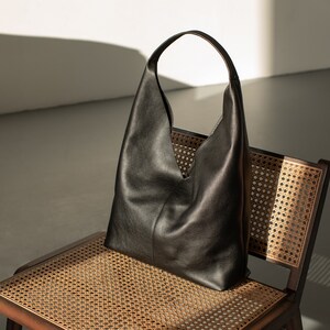 May include: A black leather tote bag with a single strap, sitting on a woven chair with a brown frame.