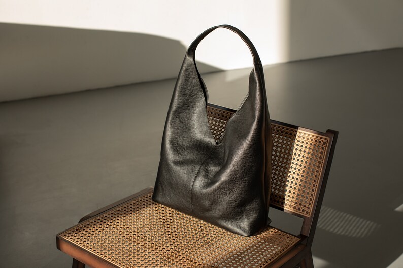 May include: A black leather tote bag with a single strap, sitting on a woven chair with a brown frame.