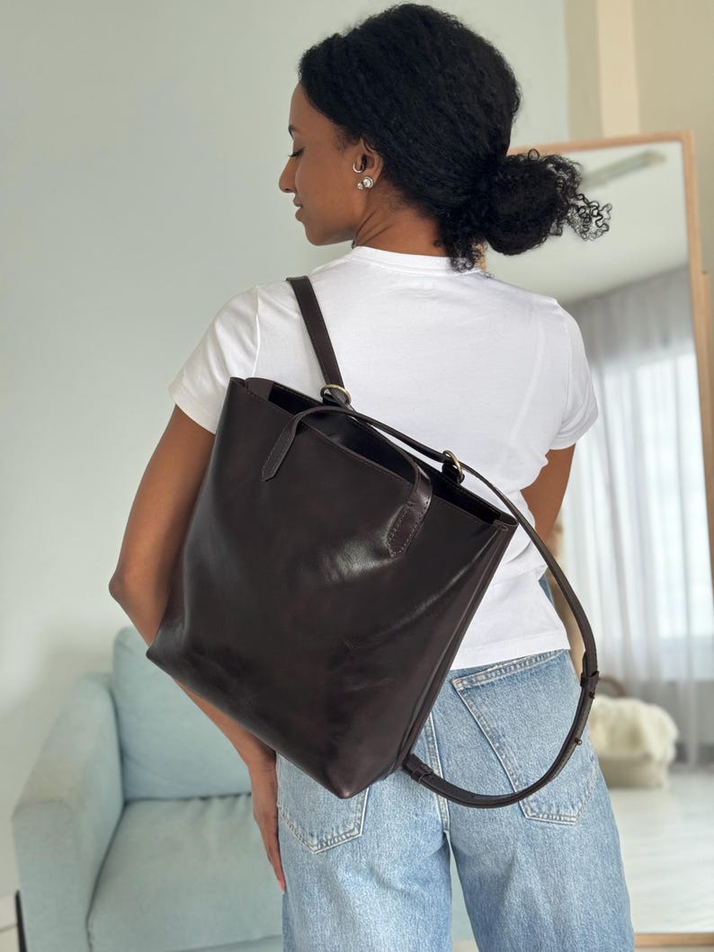 May include: A brown leather tote bag with adjustable straps that can be worn as a backpack. The bag has a top zipper closure and a spacious interior.
