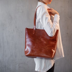 Puede incluir: Un bolso tote de cuero marr&oacute;n con una camisa blanca.