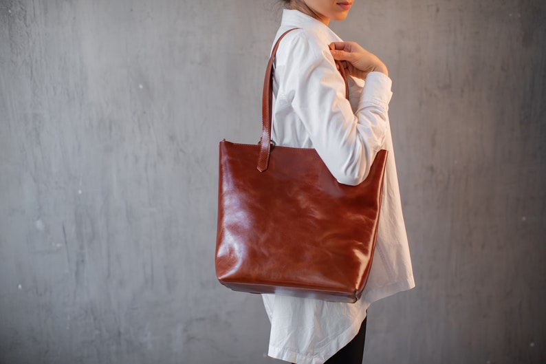 Puede incluir: Un bolso tote de cuero marr&oacute;n con una camisa blanca.