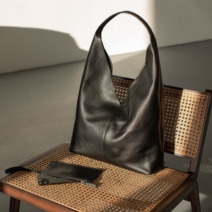 May include: A black leather tote bag with a wide, open top sits on a woven chair. A smaller black leather pouch is also on the chair.