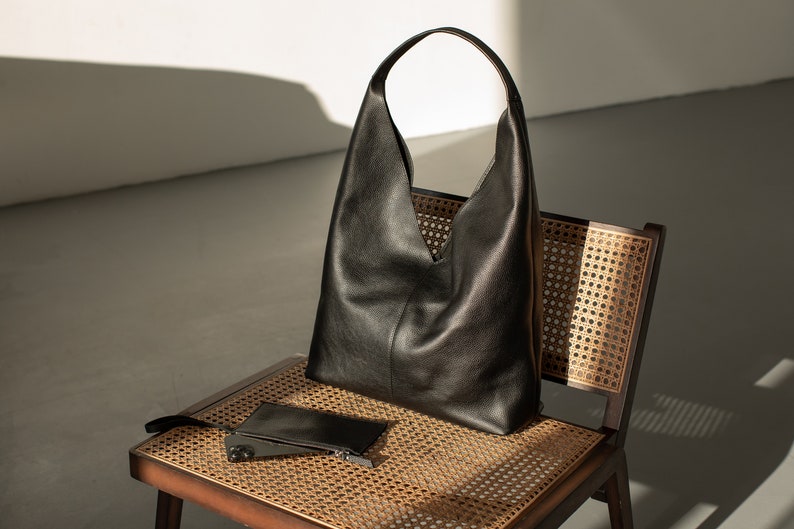 May include: A black leather tote bag with a wide, open top sits on a woven chair. A smaller black leather pouch is also on the chair.