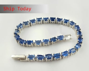 May include: A silver bracelet with a row of oval-shaped blue gemstones. The bracelet has a clasp closure.