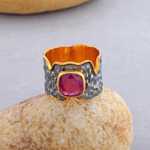 Puede incluir: Un anillo de plata con una banda texturizada y un acento dorado. El anillo presenta una gran piedra preciosa rosa de forma cuadrada.