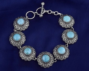 May include: A silver bracelet with a toggle clasp and six round turquoise stones set in ornate silver frames.