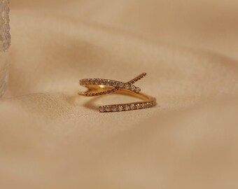 Puede incluir: Un anillo de oro con un diseño de cruz, acentuado con pequeñas piedras transparentes.