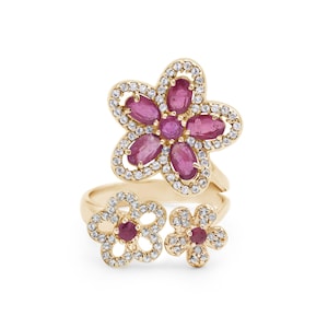Puede incluir: Anillo de oro con tres diseños de flores. La flor más grande tiene piedras preciosas rosas y piedras preciosas blancas más pequeñas. Las dos flores más pequeñas tienen piedras preciosas rosas y piedras preciosas blancas más pequeñas.