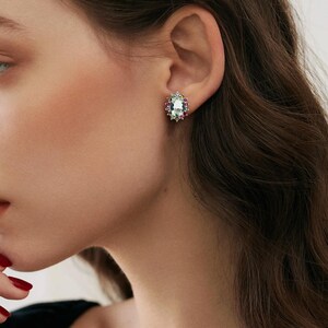 May include: Oval-shaped aquamarine gemstone earrings with a halo of smaller colorful gemstones, set in gold.